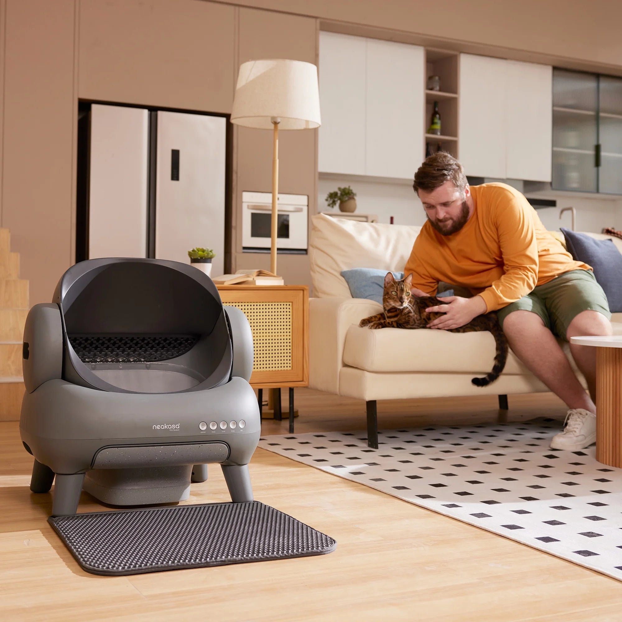 Neakasa automatic self-cleaning litter box in a modern living room while cat owner relaxes with his Bengal cat.